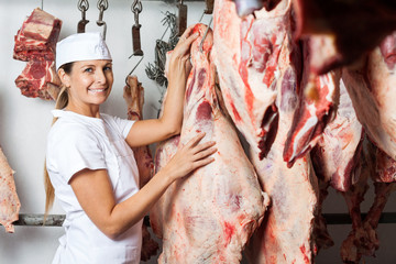 Butcher Standing By Meat Hanging In Butchery