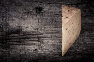 piece hard cheese with herbs on an old wooden table. tinted