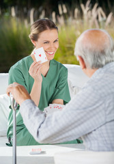 Smiling Female Caretaker Showing Ace Card To Senior Man