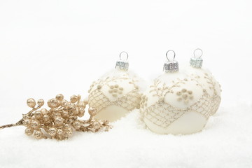 Many white christmas baubles with gold decoration on snow