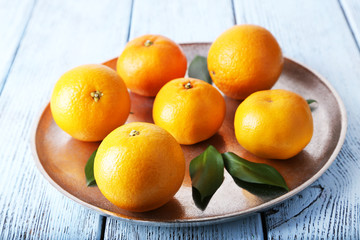 Tangerines with leaves on plate on wooden background
