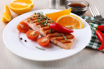 Grilled salmon and vegetables on plate on wooden background