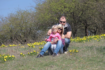 Naklejka na ściany i meble Happy mother, father and daughter in the park with yellow flower