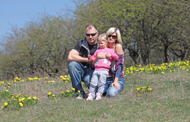 Fototapeta premium Happy mother, father and daughter in the park with yellow flower