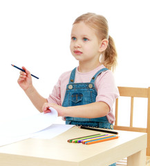 Little girl draws pencils sitting at the table.