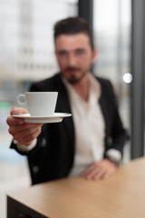 Fototapeta na wymiar Junger Geschäftsmann reicht Kaffeetasse Hochformat