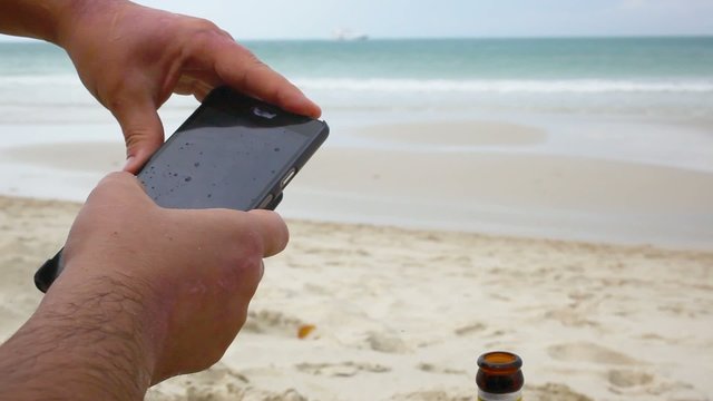Close up of man using smart phone on a beach in the rain and