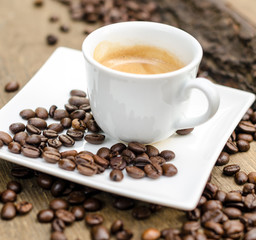 A cup of espresso and coffee beans on old wooden board