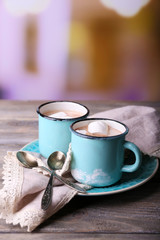 Cups of tasty hot cocoa, on wooden table, on light background