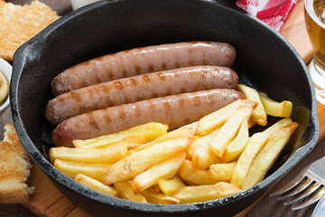 grilled sausages with French fries in a frying pan