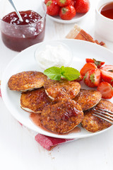 Pancakes with fresh strawberries on a plate, jam and tea