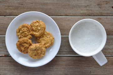 Cookies in white plate and fresh-milk on wooden table, top view.