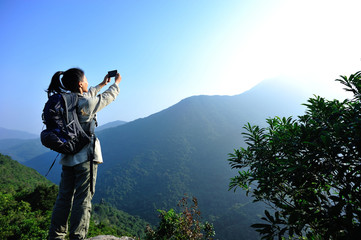 Fototapeta na wymiar woman hiker taking photo with smart phone at mountain peak 