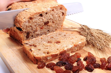 Slicing fresh bread, ears of wheat and raisins