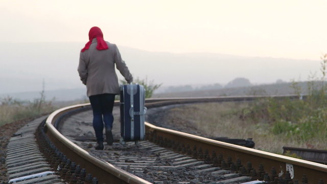 Woman passenger with luggage walking along train track