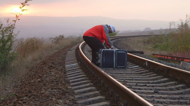 Tired passenger with suitcases sitting on railroad track
