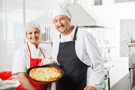 Confident Chefs With Pizza Pan At Commercial Kitchen