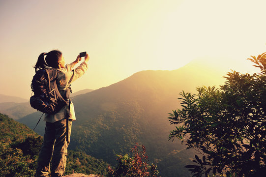 woman hiker taking photo with smart phone at mountain peak  