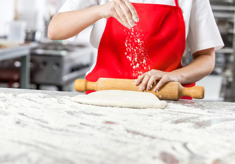 Chef Sprinkling Flour While Rolling Dough At Messy Counter