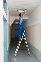 Electrician On Stepladder Installs Lighting To The Ceiling