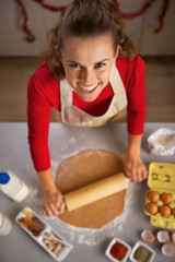 Portrait of happy young housewife rolling dough in kitchen