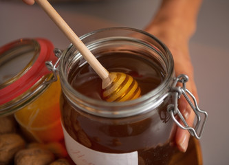 Closeup on young housewife putting honey dipper in honey jar
