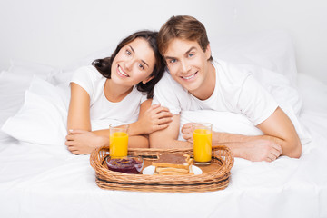Happy couple in bed having breakfast
