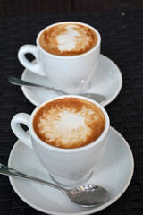 Two cups of hot cappuccino on the black background