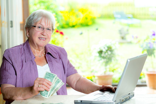 Older Woman With Money And Computer Looking Friendly