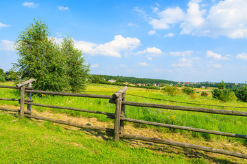 Wooden fence on green field in summer landscape of Poland