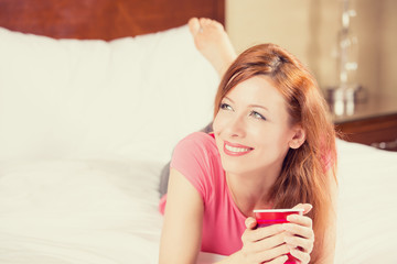 smiling woman lying in bed drinking her morning coffee