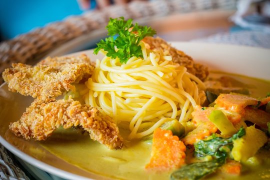 close-up of spaghetti green curry with fried pork on table.
