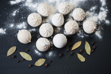 Raw khinkali with bay leaves and pepper, black wooden background