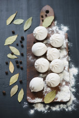 Rustic cutting board with raw khinkali and ingredients, close-up