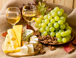 Obraz na płótnie Canvas White wine with cheese, walnuts and grapes on sackcloth