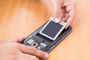 hand holding battery and smartphone on wood background