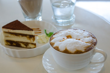 cup of cappuccino in a white cup with tiramisu cake on table