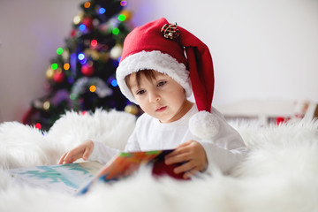 Cute adorable boy reading a book in front of the christmas tree