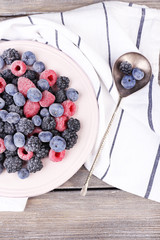 Iced berries on plate, on color wooden background