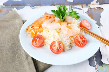 Boiled rice and shrimps, salmon on plate, on wooden background
