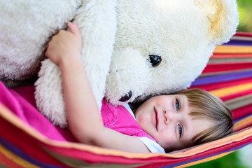 Little cute girl lying on hammock with large teddy bear