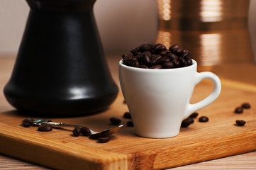 Cezve and coffee cup with heap of coffee beans on wooden board