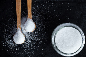 sugar in wooden spoons and glass jar on black background