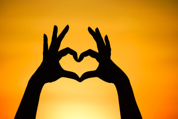 hand forming a heart shape with sunset silhouette