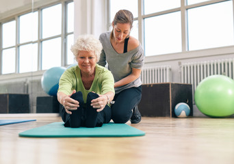 Elderly woman being helped by her instructor in the gym - Powered by Adobe