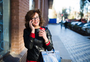 Modern young woman with coffee cup in hand talking on the mobile