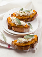 Bruschetta with pumpkin puree, ricotta and sage on a white plate