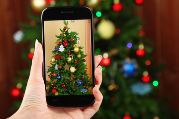Hand taking photo of Christmas tree by smartphone