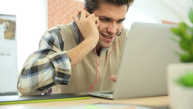 Young office worker using headphones in front of laptop