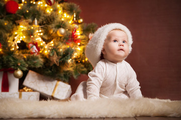 Happy baby wearing Santa hat over christmas tree